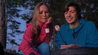 Akşam ormanında şenlik ateşinde çift marşmelov kızartıyor.