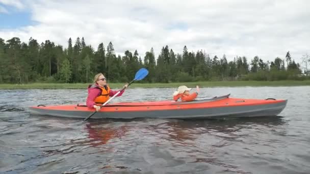 Lady in glasses rows kayak with daughter sailing along lake — Stock Video
