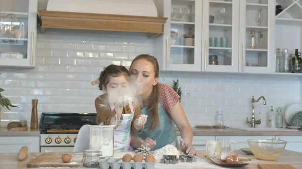 La figlia soffia farina bianca divertendosi con la madre in cucina — Foto Stock