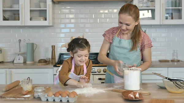 Daughter pours flour on wooden table from cup to cook pie — Stock Photo, Image