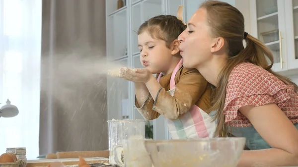 Little girl and mother blow off flour having fun in kitchen — Stock Photo, Image