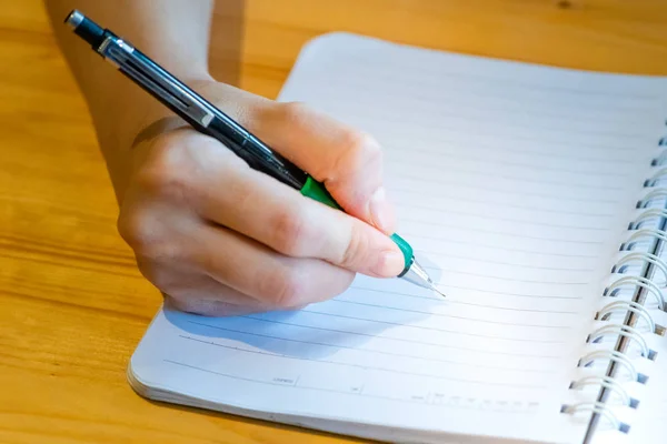 Vrouwelijke hand met potlood schrijven op notebook bij Coffee Shop. vrouw — Stockfoto