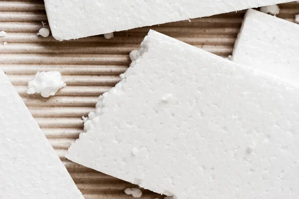 Closeup white polystyrene foam on corrugated paper. Polystyrene foam is cushioning material in packaging, material for craft applications and other.