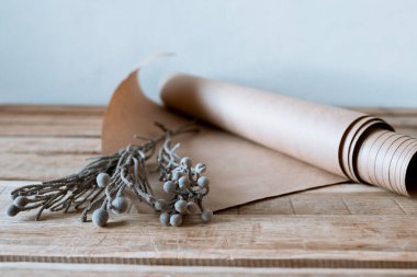 Gümüş bir fiyonk, ahşap bir masa üzerinde kağıt ve çiçekli bir hediye.