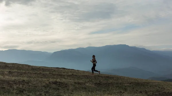 Silhouette of slim girl is jogging in foggy mountains