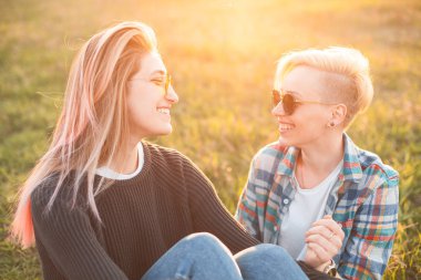 Günbatımı altında çimlerde oturan iki genç kadın,