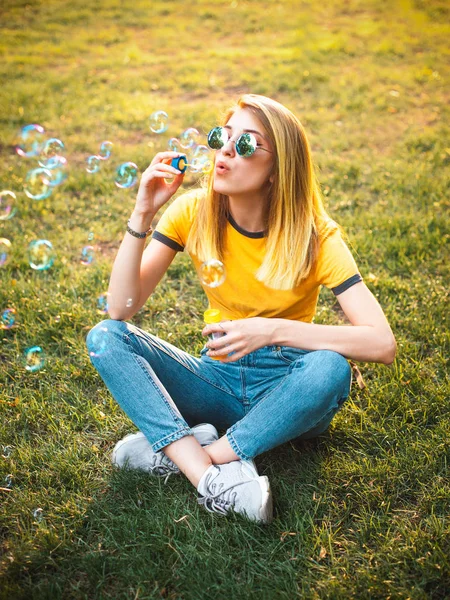 Mujer Joven Elegante Sentada Hierba Soplando Burbujas Jabón Parque — Foto de Stock