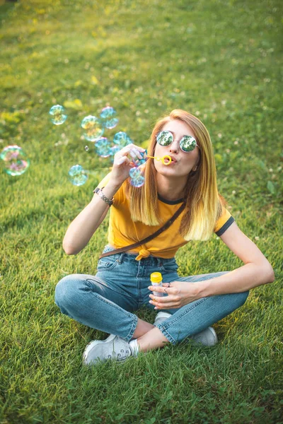 Stijlvolle Jongedame Zittend Gras Het Blazen Van Zeepbellen Park — Stockfoto