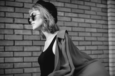 Genç kadın tuğla duvara yakın yürüyor. Siyah ve beyaz