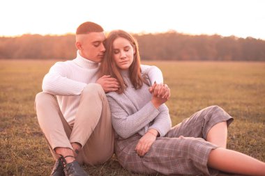 Genç adam ve günbatımı son ışığı altında çimlerde oturan kadın