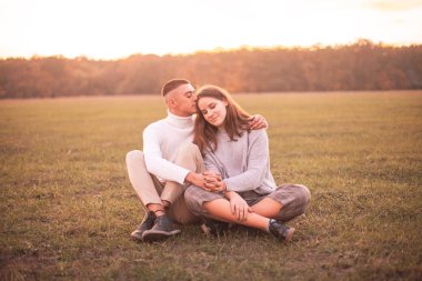 Genç adam ve gün batımının ışığı altında çimenlikte oturan kadın