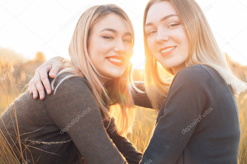 Two cheerful young women on the field at sunset. Close up