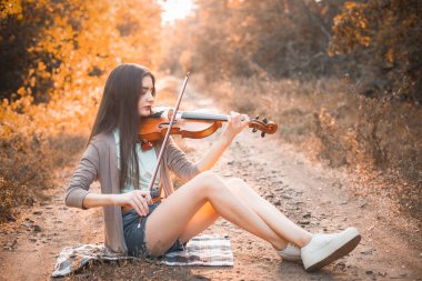 Genç kadın sonbahar ormanın içinde keman çalıyor