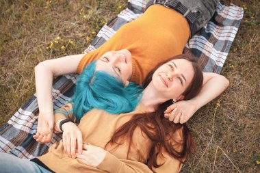 İki kadın çim üzerinde yatıyor ve gülümsüyor.