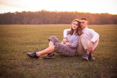 Gün batımında çim alanında oturan genç kadın ve adam