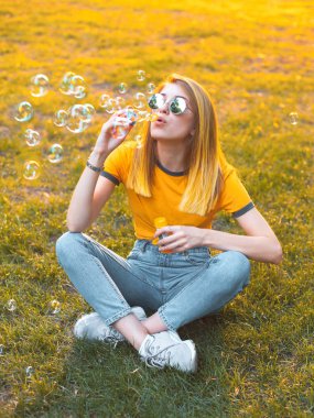 Genç bir kadın çim üzerinde oturur ve gün batımında sabun kabarcıkları darbeler