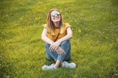 Akşamları çim üzerinde oturan neşeli genç kadın.