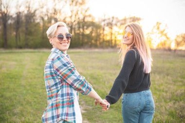 İki çekici genç kadın gün batımında sahada yürüyor. En iyi dostlar