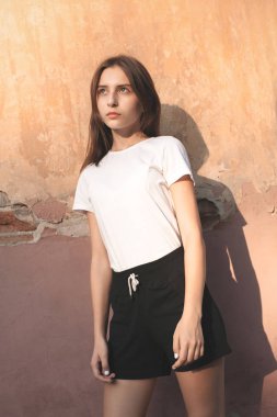 Güneş ışığında duvarın yanında duran güzel kadın.