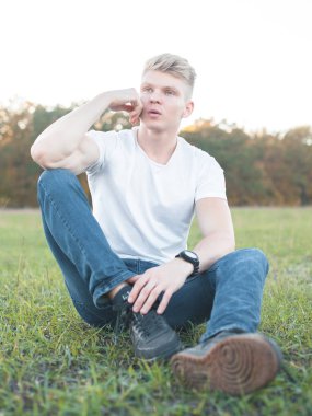 Genç adam çimlerin üzerinde oturuyor.