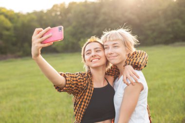 Açık havada akıllı telefonda selfie yapan iki neşeli genç kadın.