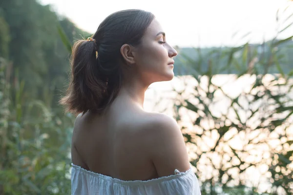 Beautiful young woman stands near the lake in the evening