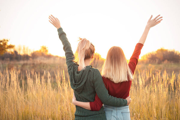 Two young women standing on the field and rise up hands at sunset.