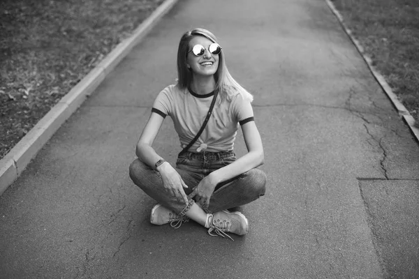 年轻女子坐在人行道上微笑着 黑色和白色 — 图库照片