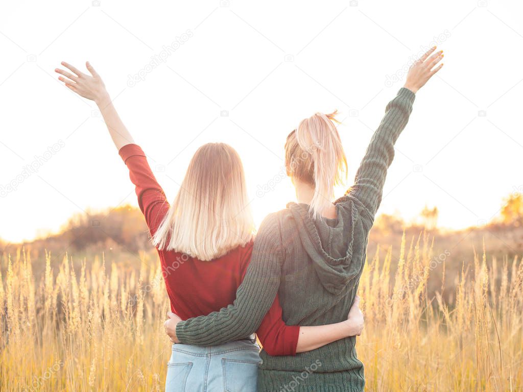Two young women standing on the field and rise up hands. Best friends