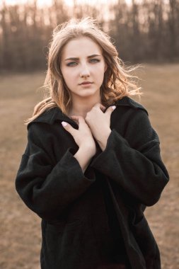 Siyah pelerinli genç bir kadın sahada yürüyor.