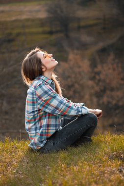 Tepede oturan neşeli genç kadın. Profil