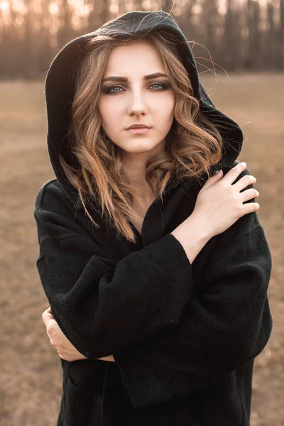Young woman in black cape walking on the field