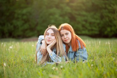 İki genç kadın güneş ışığında çimenlerin üzerinde yatıyor.