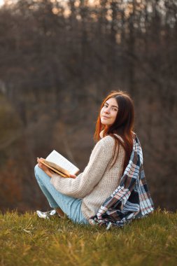 Genç bir kadın dışarıda oturur ve akşamları kitap okur. Dön.
