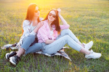Gün batımında çimenlerin üzerinde oturan iki kız.