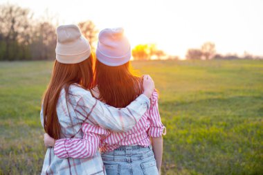 İki genç kadın sahada durup gün batımına bakıyor.