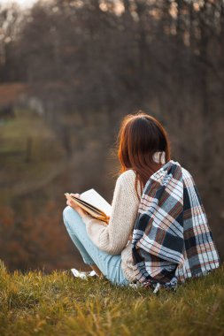 Genç bir kadın dışarıda oturur ve akşamları kitap okur. Geri görünüm