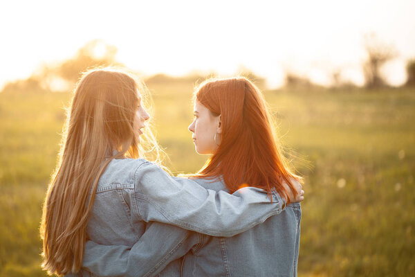 Two young women standing together under sunset. Best friends