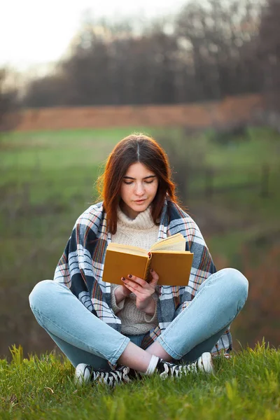 若い女性が丘の上に座って本を読んでいる ストック写真