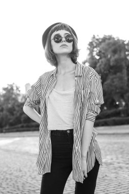 Sokakta yürüyen güneş gözlüklü, modaya uygun genç bir kadın. Siyah ve beyaz