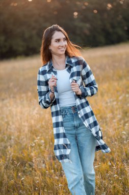 Mutlu genç kadın gün batımında sahada yürüyor.