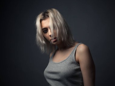 Gri arka planda üzgün genç bir kadının portresi. Yüzünde saç var..