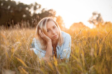 Sevimli genç kadın gün batımında kuru çimenlerde uzanıyor..