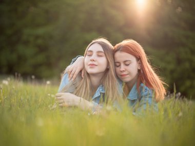 İki kız gün ışığı altında çimlerin üzerinde yatıyor. Gözler kapalı