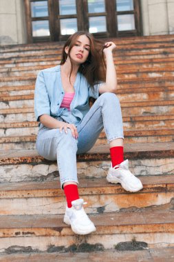 Eski paslı merdivenlerde oturan kot pantolonlu güzel genç kadın.