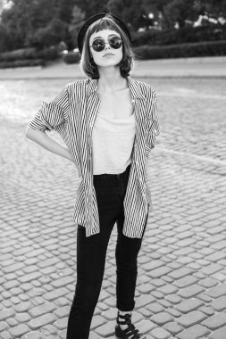 Sokakta yürüyen güneş gözlüklü, modaya uygun genç bir kadın. Siyah ve beyaz