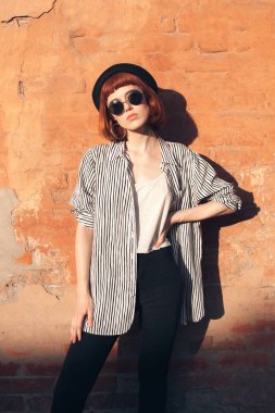 Çizgili gömlekli genç kadın duvarın yanında duruyor.
