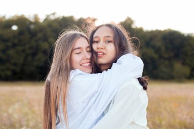 Açık havada sarılan iki beyaz gömlekli genç kadın. En iyi arkadaşlar