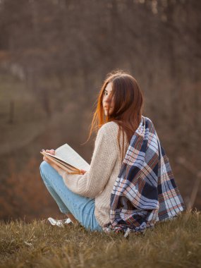 Güzel genç bayan dışarıda kitap okuyor ve arkasını dönüyor..
