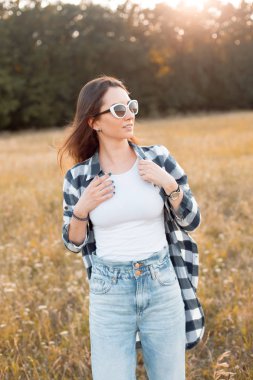 Güneş gözlüklü güzel kız gün batımında dışarıda yürüyor.